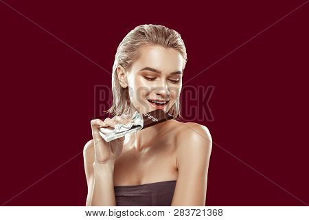 Young Model Smiling While Biting Piece Of Dark Chocolate