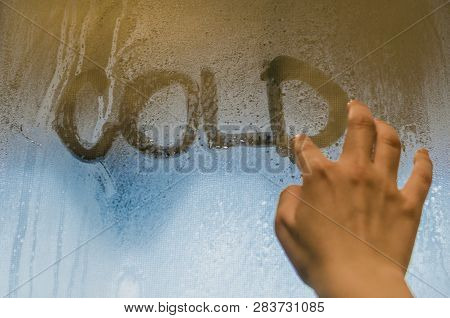 Human Hand Writing Word Cold On The Foggy Window. Water Droplets Condensation Background Of Dew On G