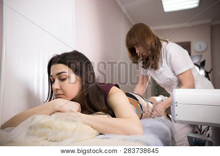 Cosmetology Beauty Clinic. Young Brunette Woman Taking Myostimulation And Doctor Preparing The Proce