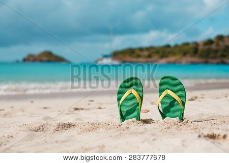 Green Flipflops In The White Sandy Beach Near Sea Waves, Nobody. Summer Vacation Concept With Blue W