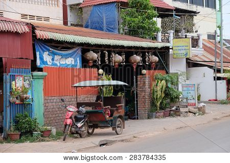 Cambodia, Siem Reap 12/08/2018 A Little Asian Girl Sits In A Moto Rickshaw Near A House With Red Lan