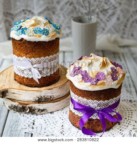 Two Traditionally Baked Orthodox Paskas With Glace Icing And Bright Blue And Violet Flowers On White