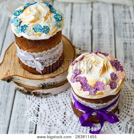 Two Traditionally Baked Orthodox Paskas With Glace Icing And Bright Blue And Violet Flowers On White