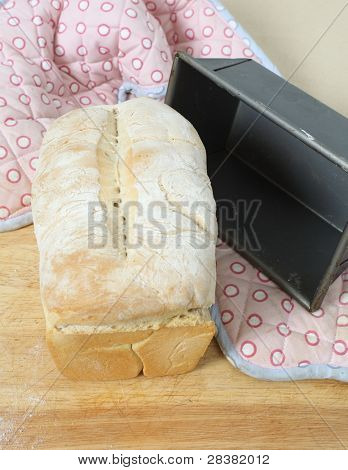 Um naco de pão inglês de split-lata, fresco do forno, sobre uma tábua de madeira com a lata de cozimento e ov