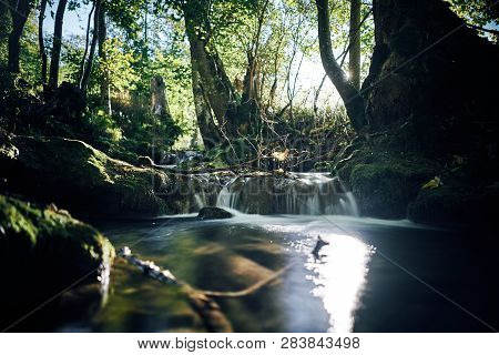 Long Exposure Of A River Creek With A Small Waterfall. Sunset And Strong Detail Bokeh View. Blue Cal
