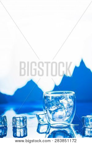 Double Wall Glass Of Clear Water On A Cold Background With Ice Cubes And Mountain Peaks. Drinking Fr