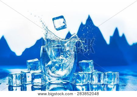 Crystal Clear Water Splash In A Double Wall Glass With Mountain Peaks On The Background. Ice Cubes I
