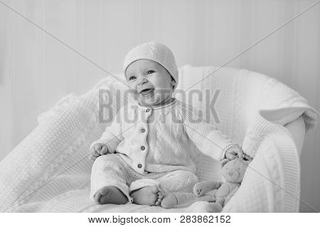 Laughing Baby Wearing Knitted Suit Is Sitting On The Chair
