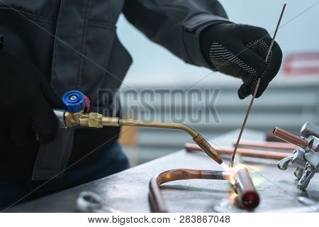 Worker Is Soldering A Pipe By A Blow Lamp On A Factory Workbench Background. Pipework.