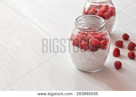 Glass Jars Of Pudding From Chia Seeds With Coconut Milk And Raspberry Berries In White Wooden Table.