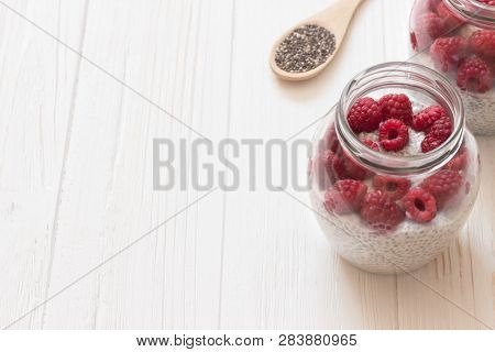 Chia Seeds Mousse With Raspberry And Coconut Milk In Glass Jars. Wooden Spoon With Chia Seeds In Whi