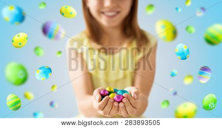 easter, holidays and people concept - close up of happy girl holding chocolate eggs in colorful foil wrappers over blue background