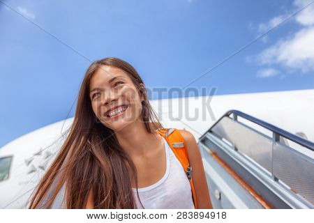 Airport travel plane arrival girl tourist arriving at destination walking out of airplane on tarmac. Happy Asian passenger woman student with backpack after plane landing at summer vacation.