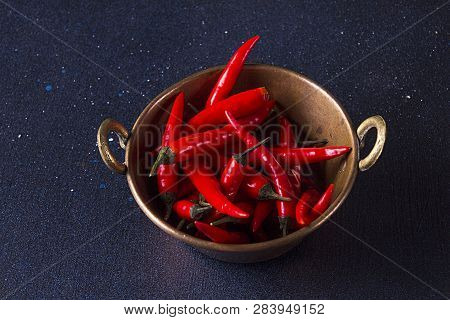 Red spisy small chili peppers in cooper bowl on dark background.