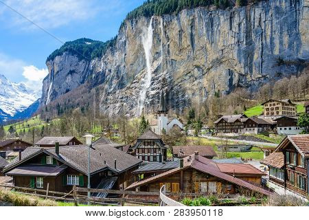 Sunny Summer View Of Amazing Touristic Alpine Village With Famous Church And Staubbach Waterfall, La