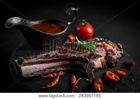 Spicy bone-in ribeye steak served with chili papper and tomato sauce on the dark background. Juicy grilled steak on black stone plate