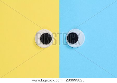 Cross-eyed Googly Eyes On Blue-yellow Background. Mad Funny Toys Eyes Close Up.