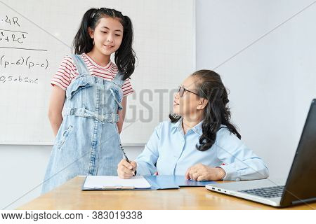 Smiling Mature Math Teacher Checking Test Results Of Schoolgirl