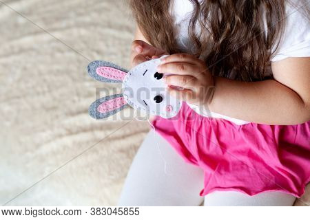 Child Girl Sews A Toy Made Of Felt Sitting On The Bed On A Beige Blanket Needlework.