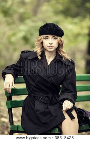 Style redhead girl sitting at bench in autumn park.