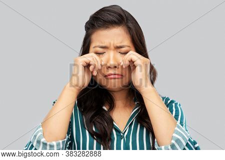 people, emotion and gesture concept - sad asian woman crying over grey background