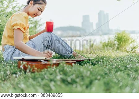Hands Hold Coffee Cup And Write Notes,lyrics In The Book On Quitar Beside The Sea And Building City 