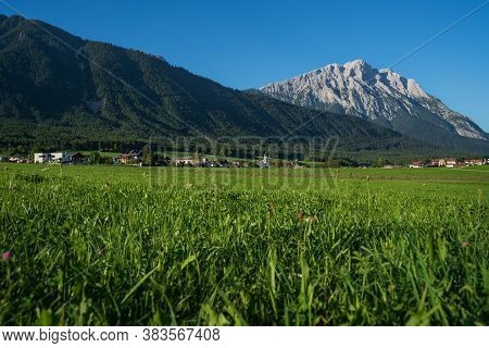 Panoramic View On Traditional Austrian Village With Alpine Rocky Mountain Range Background During Cl