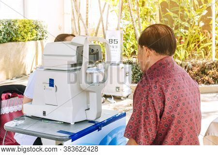 Elderly Man Checking Eye Vision On Optometry Equipment With A Mobile Hospital Unit For Eye Examinati