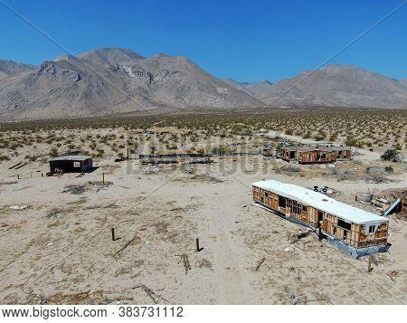 Aerial View Of Abandoned Houses And Camper Trailer In The Middle Of The Desert Under Blue Sky In Cal