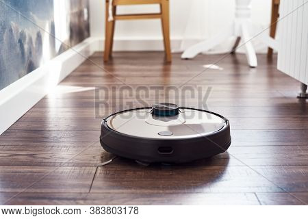 Close Up Of Robotic Vacuum Cleaner On Laminate Wooden Floor Cleaning Unert A Chair In The Kitchen. S