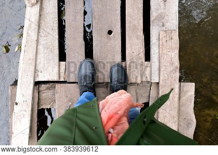 Old Wooden Bridge Over The Stream. Pants, Sneakers, Scarf, Raincoat Are Visible. View From Above