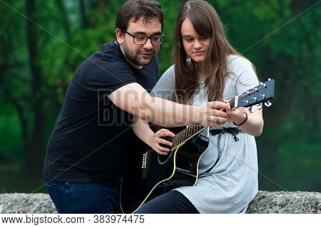 Older Brother Teaching His Younger Sister To Play Guitar In The Nature. Beautiful Moments Spent Toge