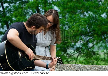 Older Brother Teaching His Younger Sister To Play Guitar In The Nature. Beautiful Moments Spent Toge