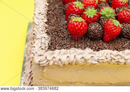 Homemade chocolate cake covered with chocolate sprinkles and fresh strawberries. Known in Brazil as Bolo de Brigadeiro. Isolated on yellow background. Close-up. Copy space.