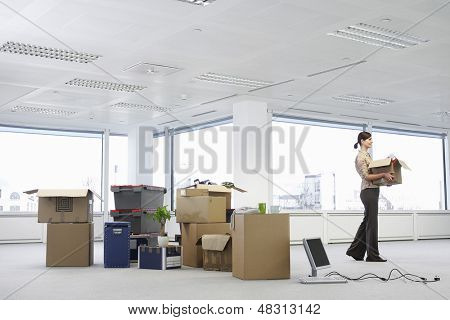 Jeune femme transportant une boîte en carton près de cartons et de matériel dans l'espace de bureau vide