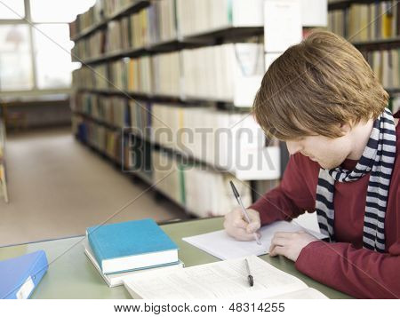 Jovem estudante masculino fazendo lição de casa na mesa na biblioteca