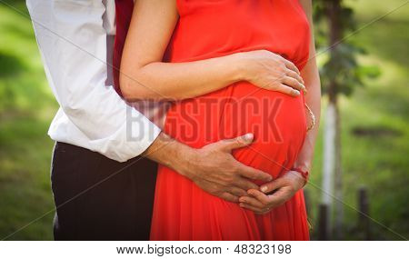 Imagem da mulher grávida e espanhol abraçando a tocar sua barriga com as mãos