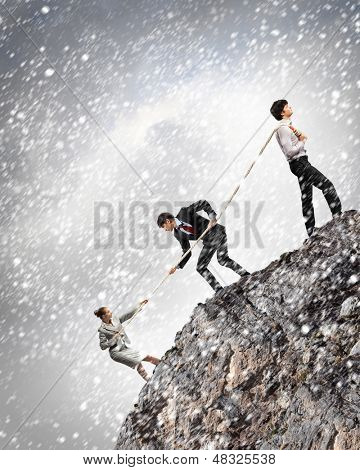 Imagem de três empresários puxando a corda no topo da montanha sob a queda de neve