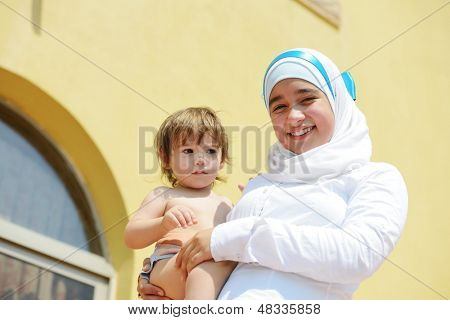 Donna musulmana tenendo un bambino piccolo a casa all'aperto