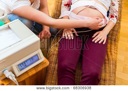 Midwife exanimating belly of pregnant woman with CTG scanning in practice
