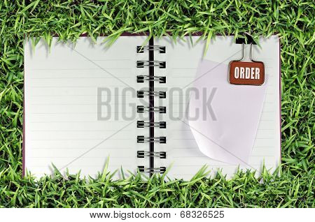 blank page of note book on grass and Binder Clip.