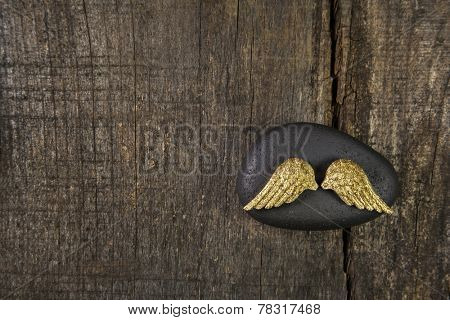 Golden angel wings with black stone on old wooden background for a card announcing somebodies death.