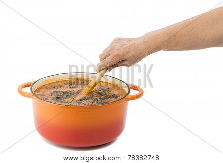 Female hand mixing lentil soup in cast iron cooking pot isolated on white background.