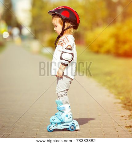two year old pretty girl in roller skates and a helmet on the street