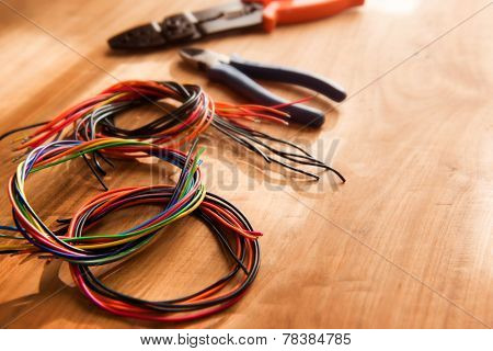 Colored cables or wires and a wire cutter tools on a wooden work desk, with by-the-window type lighting environment.