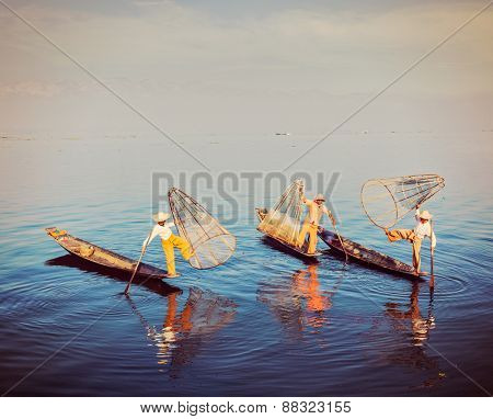 Traditional Burmese fishermen balancing with their fishing net on boats at Inle lake in Myanmar famous for their distinctive one legged rowing style. Vintage filtered retro effect hipster style image