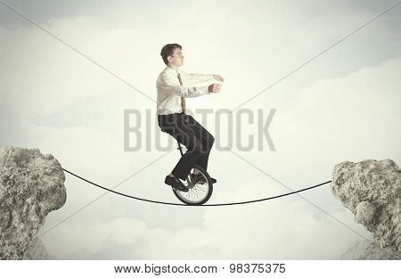 Brave business man riding an mono cycle between cliffs concept