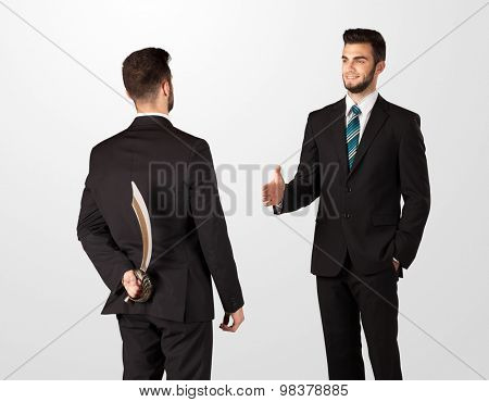 Two opposing businessman shake hands, one of them hiding a weapon behind his back