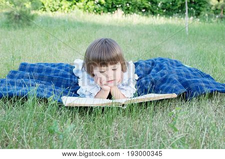 Child reading book lying on stomach outdoor smiling cute little girl children education and developmen. Kids outside activity. Back to school concept