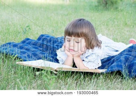 Child reading book lying on stomach outdoor smiling cute little girl children education and developmen. Kids outside activity. Back to school concept